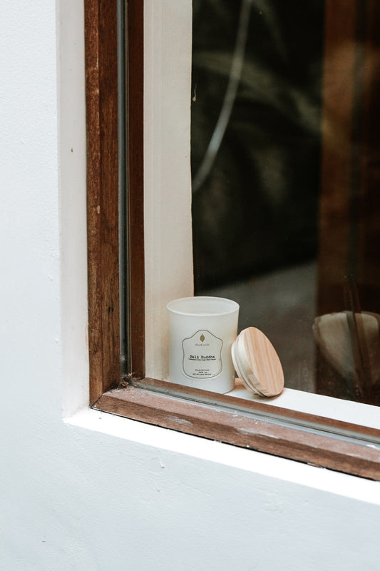 Unlit Ollie & Co. soy candle with wooden lid on a windowsill, ready for its first burn